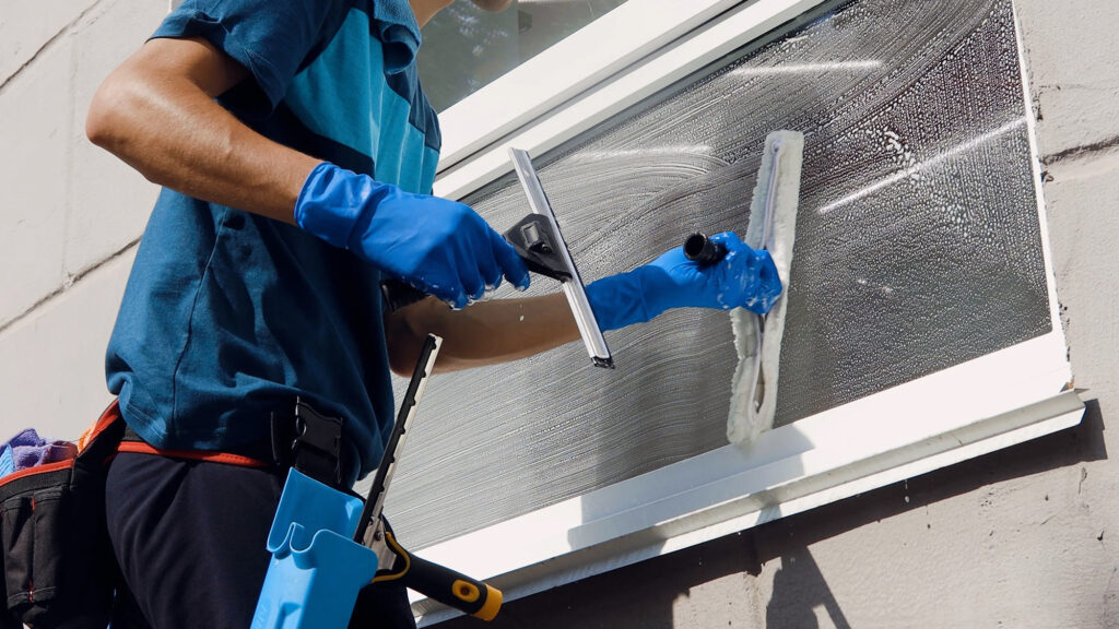 A man wearing blue gloves is cleaning a window with a cloth, focusing on achieving a streak-free shine.