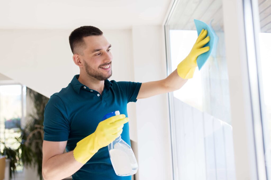 A man in rubber gloves cleans a window, using a yellow cloth to remove dirt and smudges for a clear view.